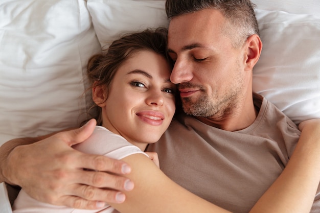 Top view of smiling loving couple lying together on bed at home