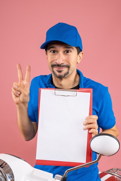 Top view of smiling male delivery person wearing hat sitting on scooter showing document making victory gesture