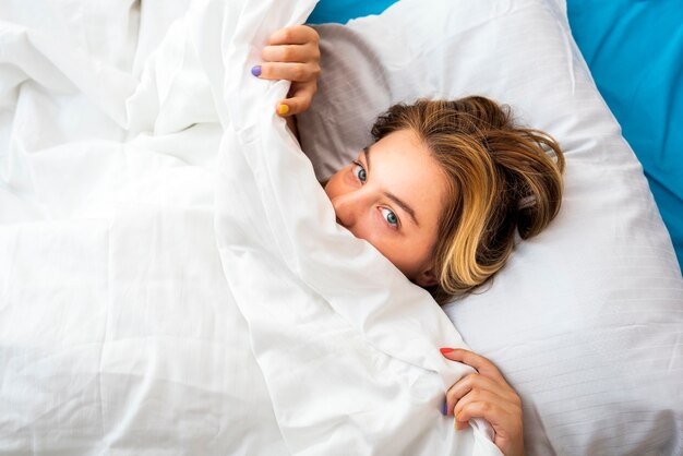 Top view smiling woman pulling the bed sheet under the nose