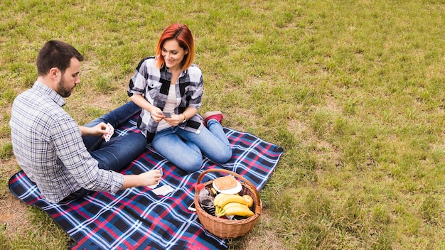 Top view of smiling young couple playing with cards on blanket at picnic