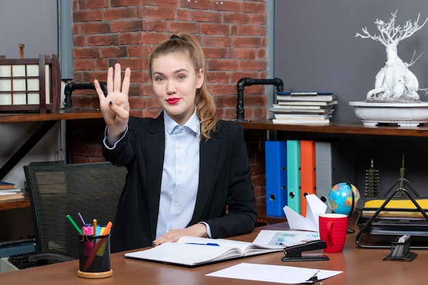 Free photo top view of smiling young female sitting at a table and showing four in the office