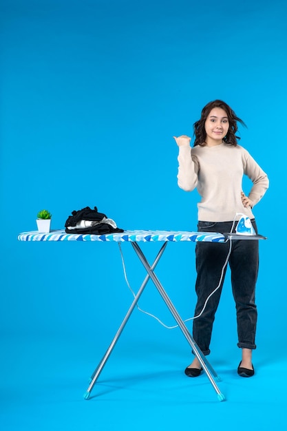Top view of smiling young girl standing behind the ironing board and pointing back on blue wave surface