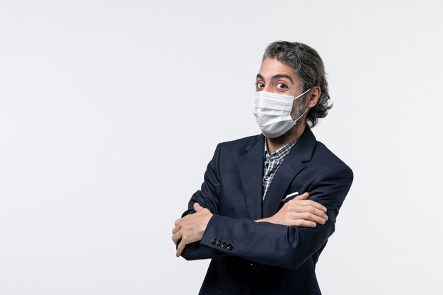 Top view of smiling young guy in suit wearing mask and shrugging his shoulder on white background