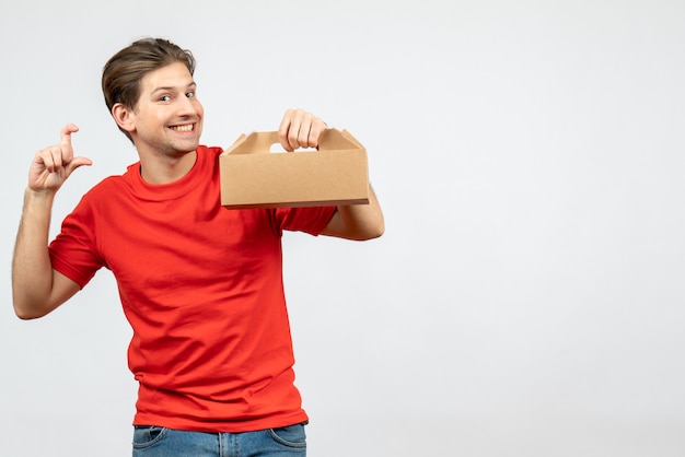 Free photo top view of smiling young man in red blouse holding box making exact something on white wall