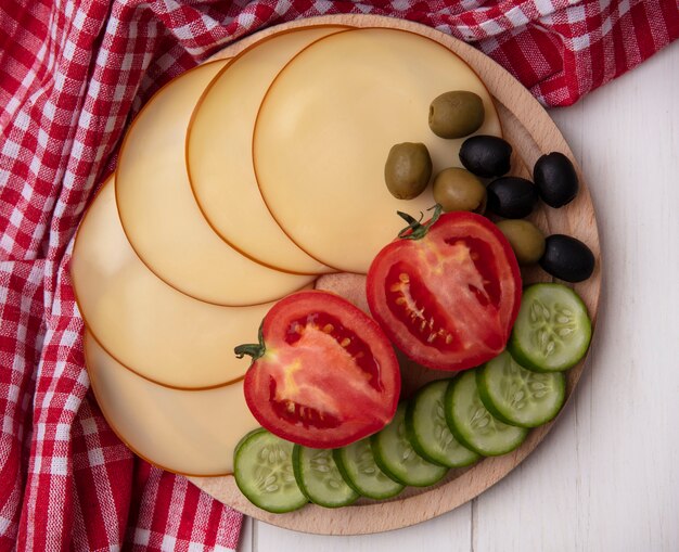 Top view smoked cheese with tomatoes  cucumbers and olives on a stand with a red checkered towel  on a white background