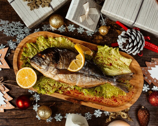 Top view of smoked fish served with lettuce and lemon in bamboo serving