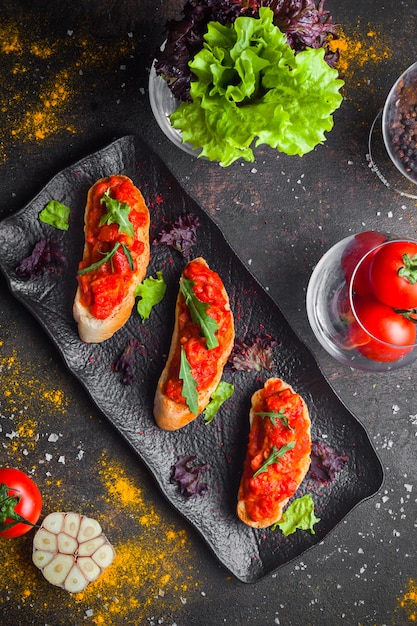 Top view snack with tomato salad and sliced bread and arugula in dark plate