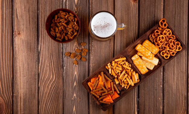 Vista dall'alto snack per birra chip chuck mini birzel e crackers salati con boccale di birra su fondo di legno