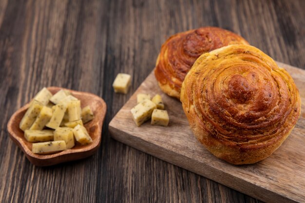 Top view of soft buns on a wooden kitchen board with chopped slices of cheese on a wooden bowl on a wooden background