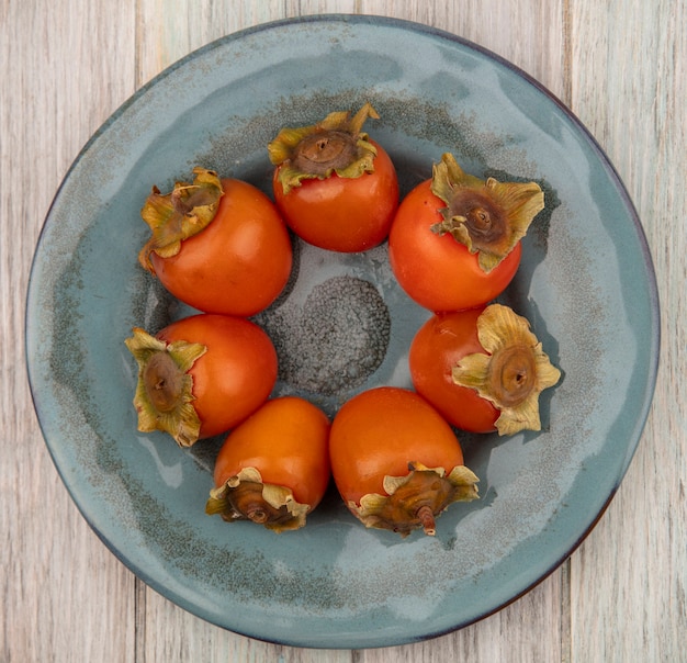 Top view of soft and juicy persimmons on a plate on a grey wooden surface