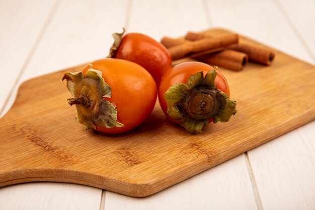 Top view of soft persimmons on a wooden kitchen board with cinnamon sticks on a white wooden surface