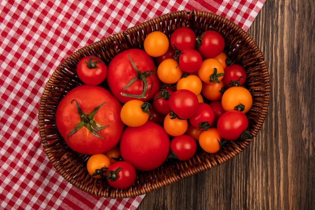 Top view of soft red and orange tomatoes on a bucket on a checked cloth on a wooden surface