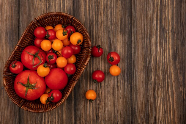 Top view of soft red and orange tomatoes on a bucket on a wooden surface with copy space