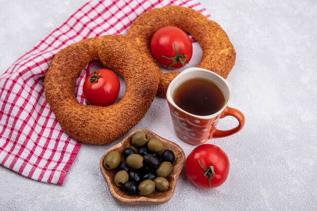 Top view of soft turkish bagels with fresh tomatoes and olives on a wooden bowl on a red checked cloth on a white background