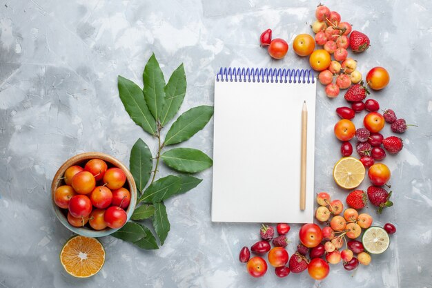 Top view sour cherry-plums with lemon and other fruits notepad on the light desk