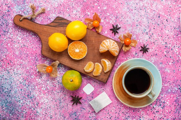 Top view of sour fresh tangerines with lemons and cup of tea on pink surface