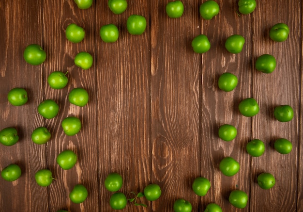 Top view of sour green plums scattered on wooden table with copy space