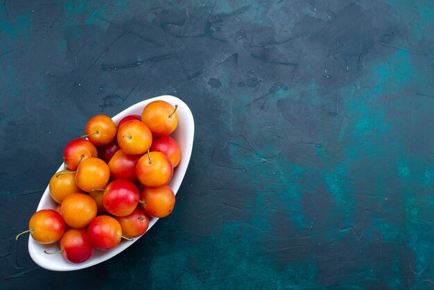 Top view of sour plums inside plate on dark-blue surface