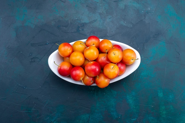 Top view of sour plums inside plate on the dark-blue surface