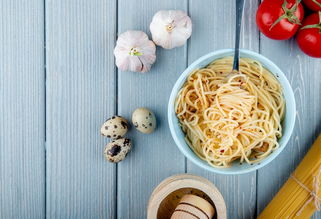 Vista superiore della pasta degli spaghetti con i fiocchi di peperoncino rosso in una ciotola bianca con le uova fresche dell'aglio e di quaglia dei pomodori della forcella su fondo rustico di legno