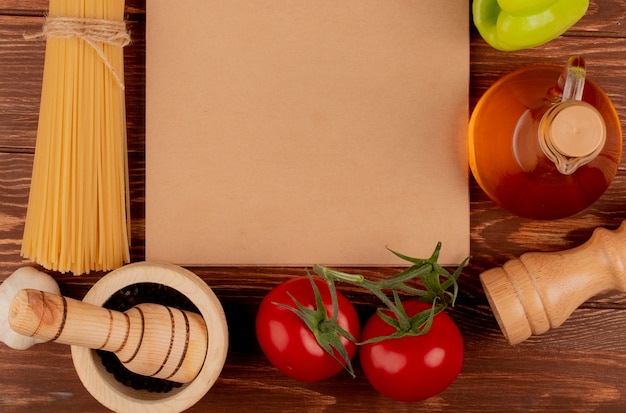 Top view of spaghetti pasta with ingredients around note pad on wooden surface with copy space