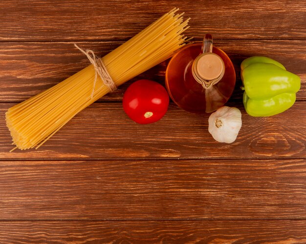 Top view of spaghetti pasta with tomato, garlic, pepper and melted butter on wooden surface with copy space