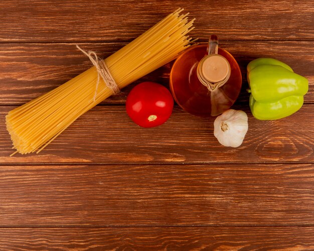 Взгляд сверху макаронных изделий спагетти с томатом, чесноком, перцем и топленым маслом на деревянной поверхности с космосом экземпляра