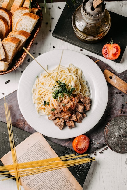 Top view of spaghetti with pieces of meat and tomato on a wooden board