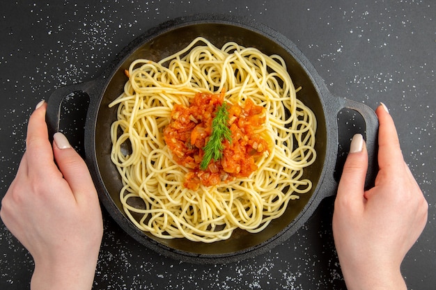 Top view spaghetti with sauce in frying pan in female hand on black table