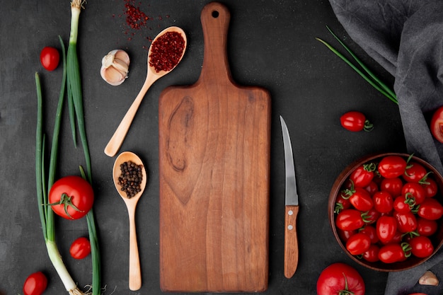 Free photo top view of spices with scallions tomatoes garlic and cutting board on black surface