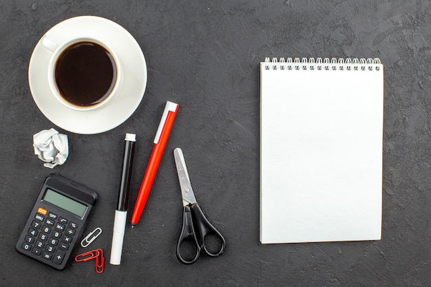 Top view spiral notepad scissors calculator cup of tea red pen and black marker on black