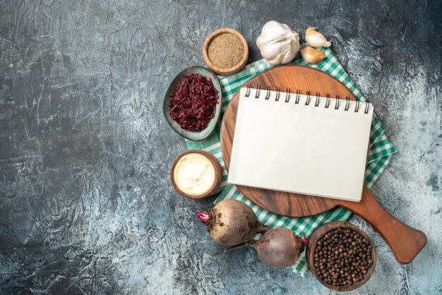 Top view spiral notepad on wood board spices in bowls garlic beets on grey table with free space