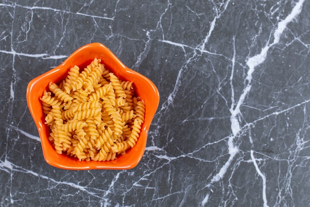 Top view of spiral pasta in orange bowl.