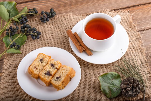 Top view of sponge cake slices on a plate with a cup of black tea on rustic background