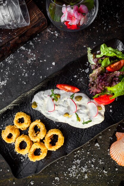 Top view squid rings in batter with sauce and fresh vegetable salad in tray