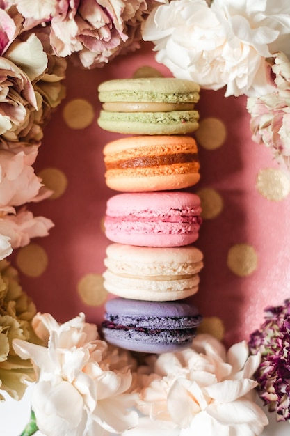 Top view of stacked colorful French macaroons and beautiful flowers on a pink background
