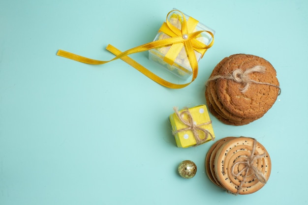 Top view of stacked various delicious cookies and beautiful yellow gift boxes on the left side on pastel green background