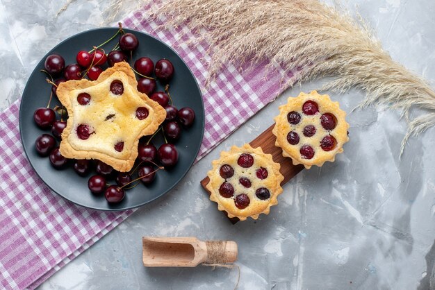 Top view star shaped cake along with cherry cakes and fresh sour cherries on the light table cake pie bake fruit color