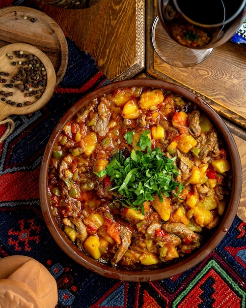 Top view of stewed beef meat with potatoes  green pappers and herbs in a clay bowl on a wooden table