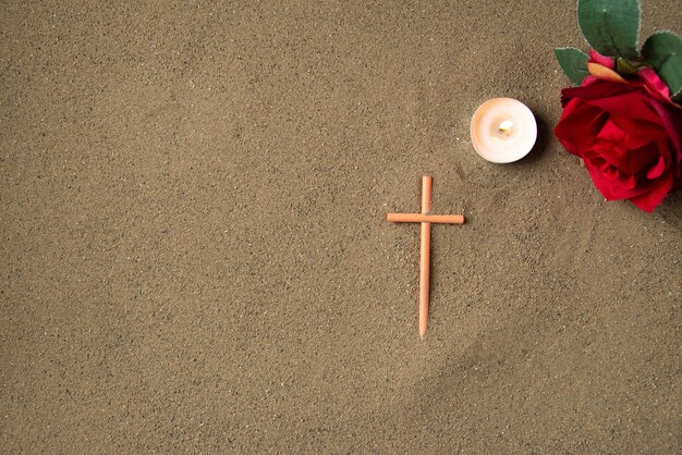 Top view of stick cross with red flowers on the sand