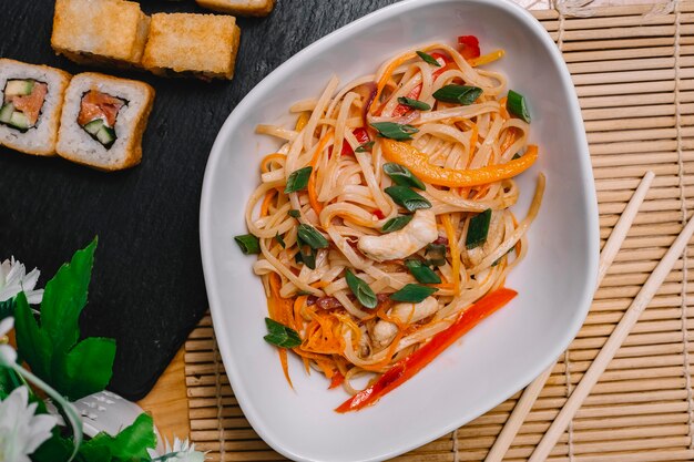 Top view stir-fried noodles with grilled chicken bell pepper and carrot with sushi roll on the table