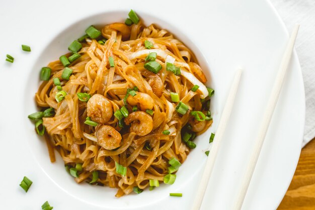 Top view stir-fried noodles with shrimps soy sauce and spring onion on a plate