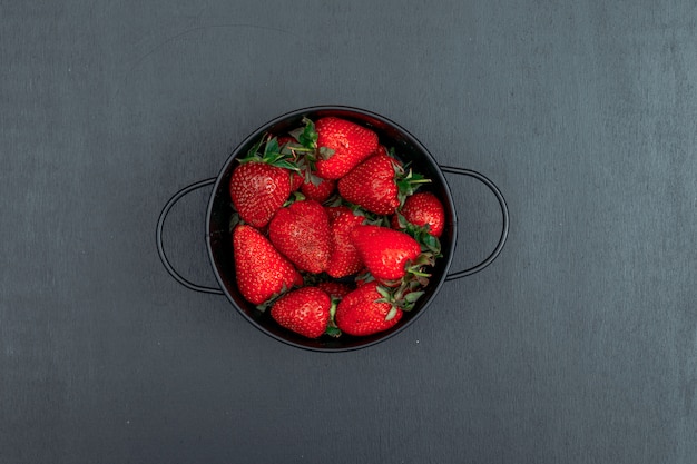 Top view strawberries in iron bowl on black background. horizontal