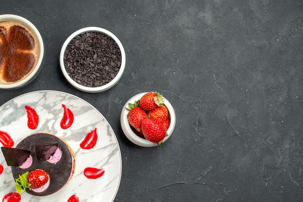 Top view strawberry cheesecake on oval plate bowls with strawberries and chocolate a cup of coffee on dark background