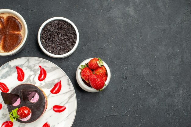 Top view strawberry cheesecake on oval plate bowls with strawberries and chocolate a cup of coffee on dark background