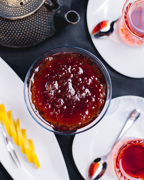 Top view of strawberry jam in a glass vase served with tea on the table