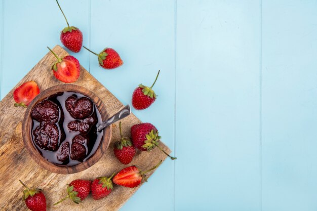 Top view of strawberry jam on a wooden bowl with fresh strawberries on a white background with copy space