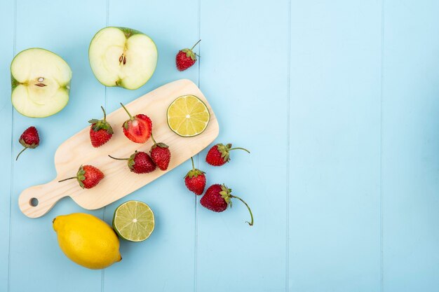 Top view of strawberry on a kitchen board with lemon and apple on a blue background with copy space