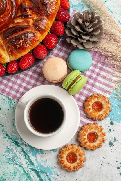 Top view strawberry pie with cookies macarons and cup of tea on blue surface