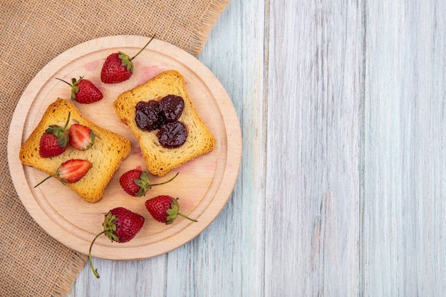 Top view of strawberry on a wooden kitchen board on a sack cloth on a grey wooden background with copy space